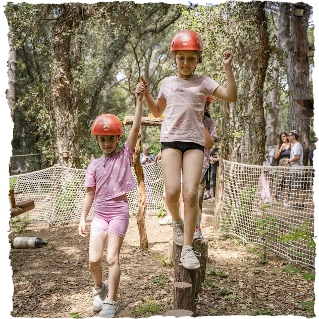 Nena ajudant a passar un obstacle a una altre al parc d'equilibri Dumbo